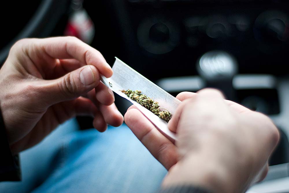 A driver rolling a marijuana joint in a car. Driving under the influence of recreational marijuana in Connecticut can lead to motor vehicle accidents.